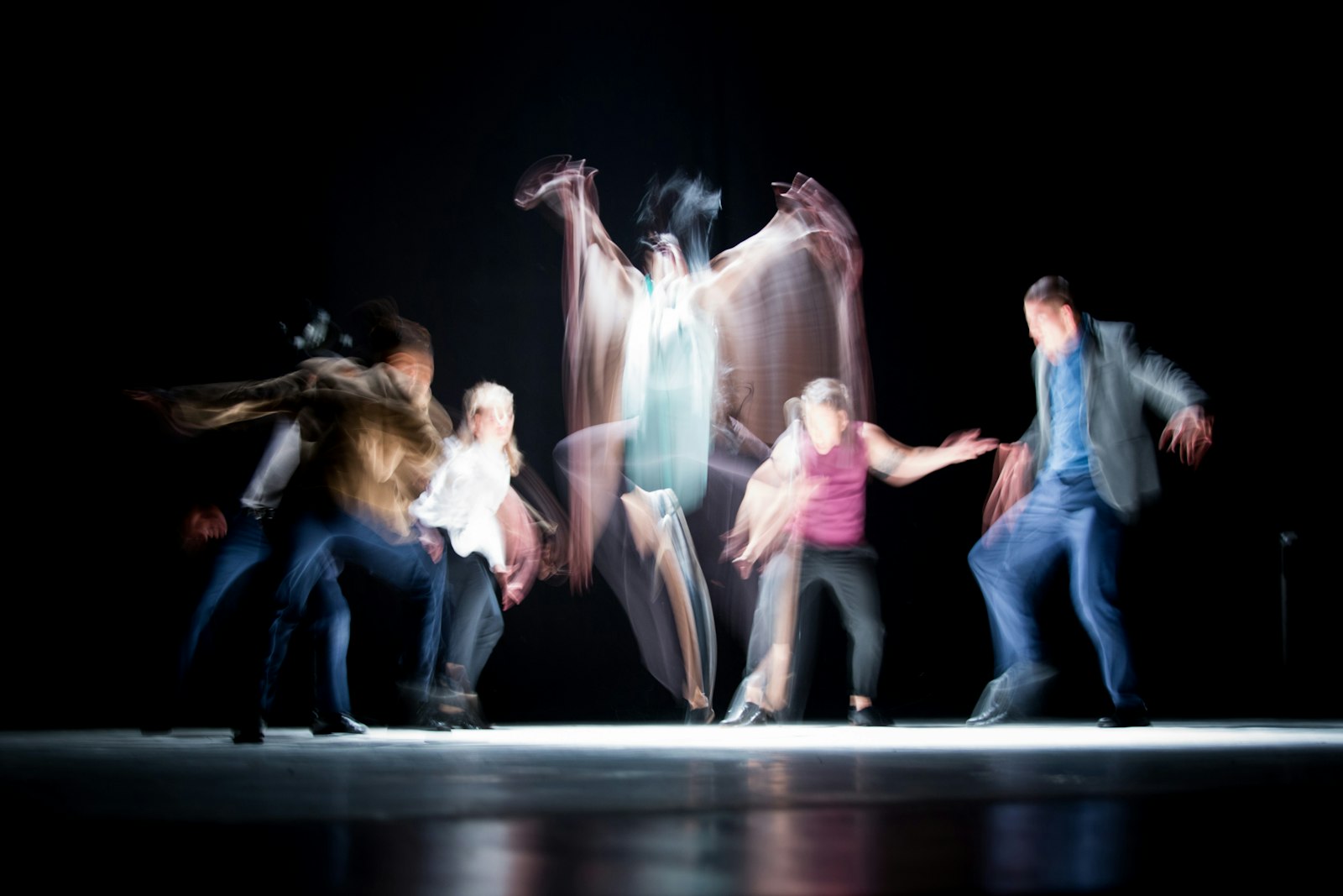 A group of dancers mid-phrase on a dark stage, captured with heavy motion blur