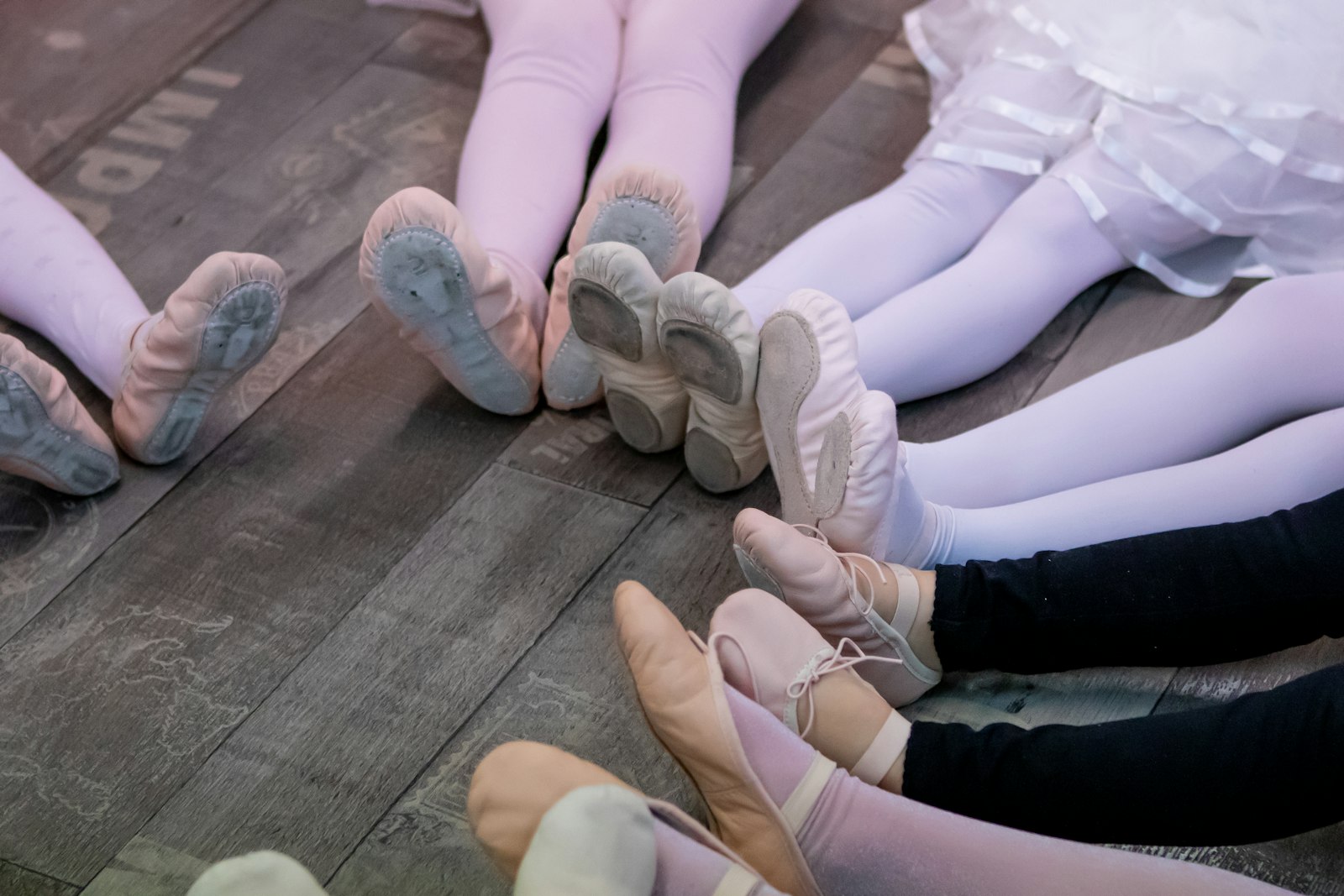 Young ballet dancers in soft shoes sitting together on a wooden studio floor