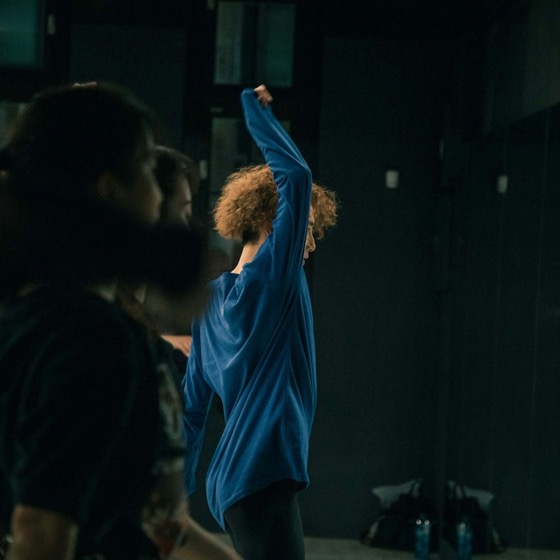 A dancer marking a move in a dark studio while others watch