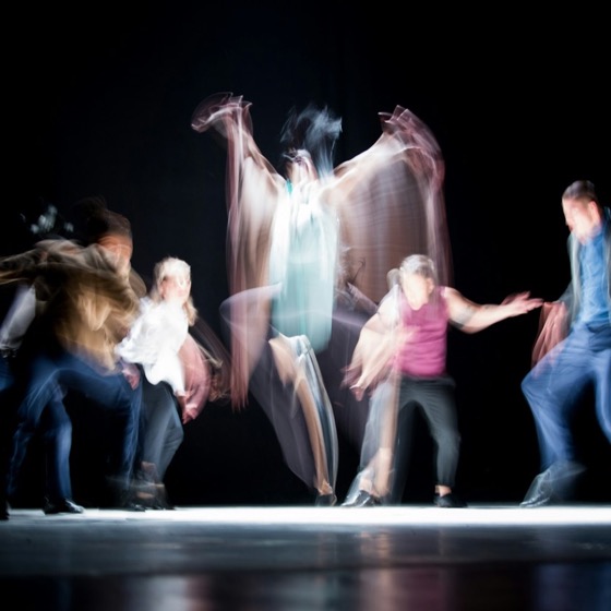A group of dancers mid-phrase on a dark stage, captured with motion blur