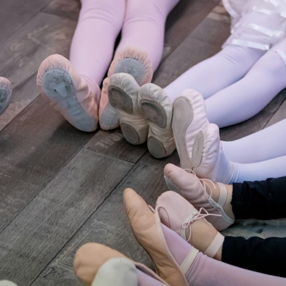 Young ballet dancers in soft shoes sitting on a wooden studio floor